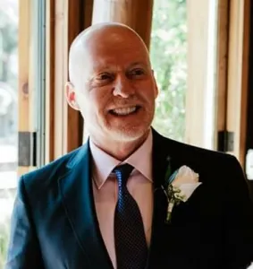 A bald man in a suit smiles at the camera.